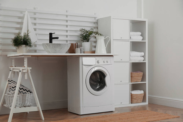 Laundry room interior with modern washing machine and shelving unit near white wall - Foto, imagen