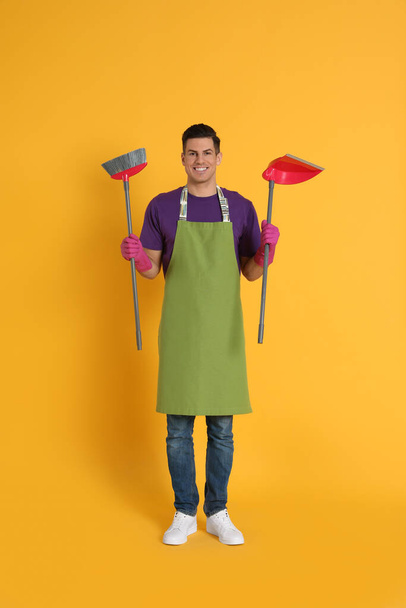 Man with broom and dustpan on orange background - Foto, afbeelding