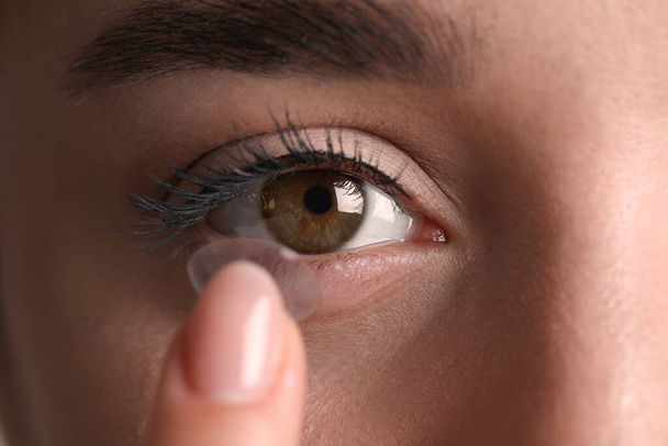 Closeup view of young woman putting contact lens in her eye - 写真・画像