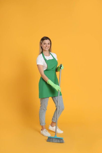 Young woman with broom on orange background - Foto, Imagem