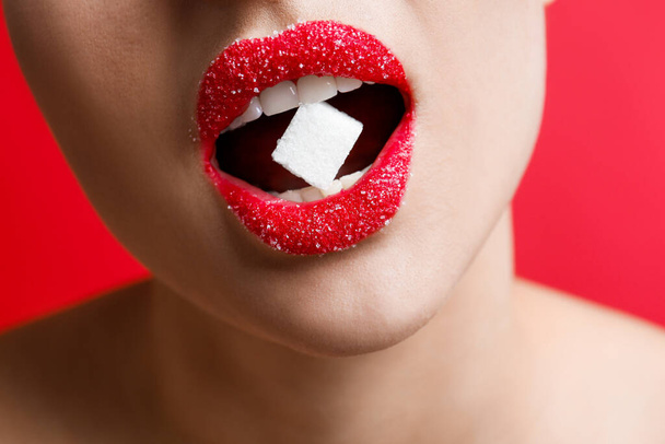 Woman with beautiful lips eating sugar cube on red background, closeup - Fotó, kép