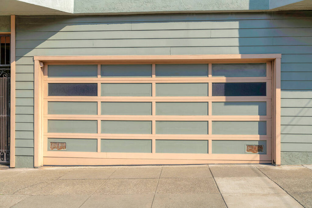 Se adjunta garaje exterior con tonos grises verdosos en San Francisco, California. Garaje con entrada de concreto y puerta de garaje seccional con rejillas beige cerca de la puerta de hierro forjado a la izquierda. - Foto, Imagen