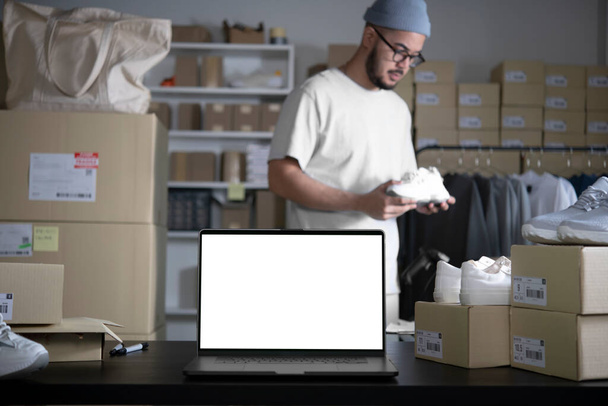 Laptop with blank white screen standing on the desktop in the warehouses. Asian man online seller checking stock and Inventory before sending to the customer. E-commerce business owner working in store warehouse. - Foto, Imagen