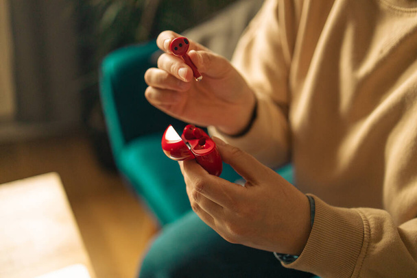freelancer mujer manos con auriculares inalámbricos rojos estancia en casa sentarse acogedor sofá sala de estar en el interior - Foto, imagen