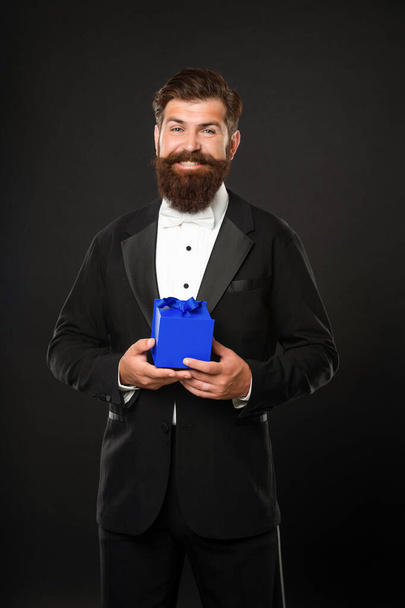 happy man in tuxedo bow tie formalwear on black background with gift box. boxing day - Zdjęcie, obraz