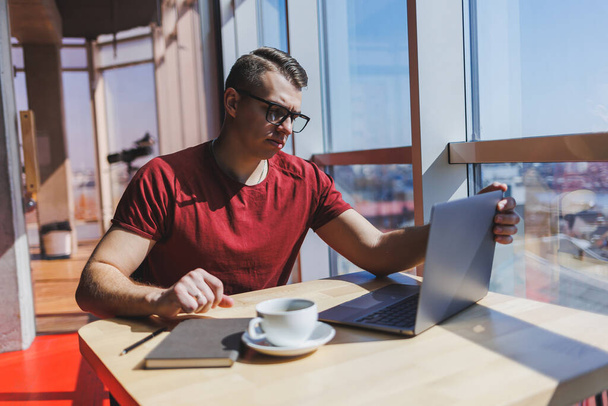 Portrait d'un homme, informaticien, travaillant à distance avec un ordinateur portable moderne, assis à une table et souriant à la caméra pendant une pause, un programmeur humain heureux dans des lunettes de correction de la vision - Photo, image