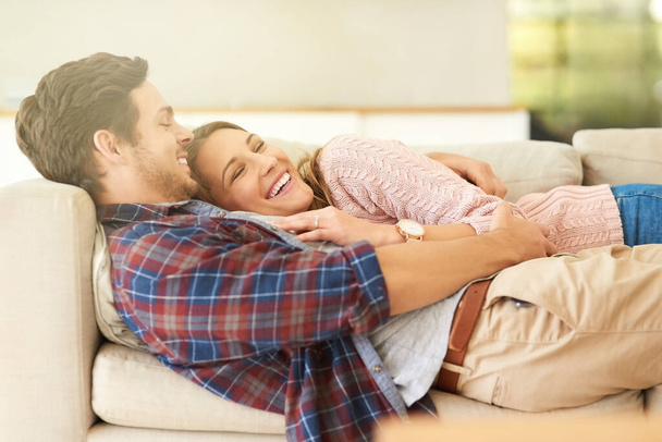 We fit together perfectly. Shot of a happy young couple relaxing on the sofa at home. - 写真・画像