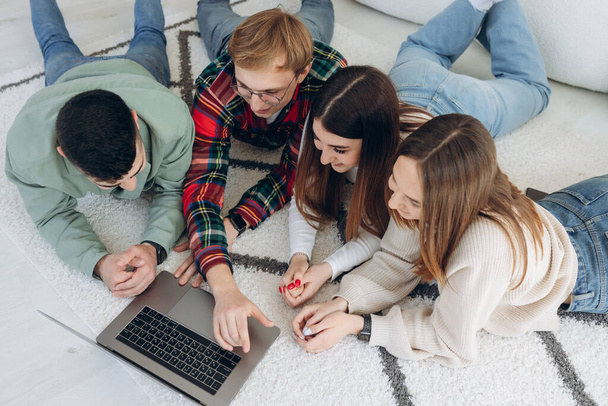 Щасливі друзі-підлітки весело проводять час разом, спостерігаючи за ноутбуком, що лежить на підлозі поруч один з одним в дизайні комфортної вітальні
 - Фото, зображення
