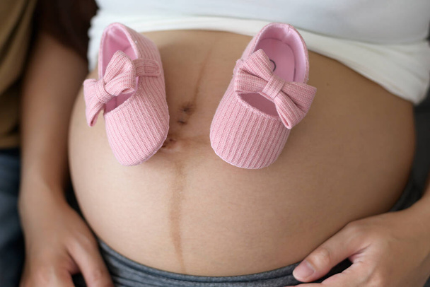 Young pregnant woman putting baby shoes on tummy, family and pregnancy care concept - Fotografie, Obrázek