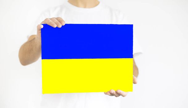 Kerel met papier in de vorm van een gele en blauwe vlag van Oekraïne op een witte achtergrond. - Foto, afbeelding