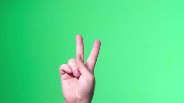 Male hand on green background shows hand sign, victory gesture.  - Imágenes, Vídeo
