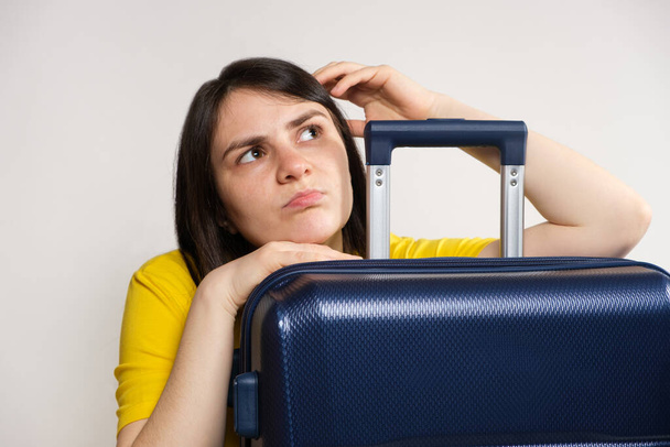 Une jeune femme européenne de 25 ans rêve de voyager embrassant une valise bleue sur un fond blanc - Photo, image