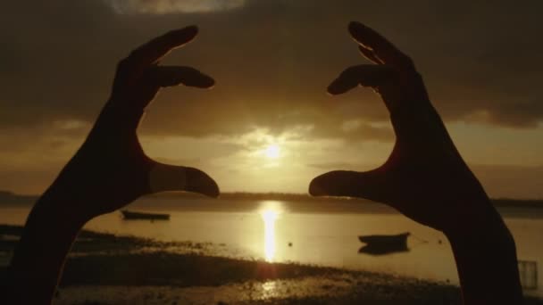 Happy girl on the beach at sunset. Figure made by fingers. Hands of girl shape of heart. Summer dream. Happiness of freedom at sunset. Sunlight between fingers. Silhouette of happy girl on the ocean - 映像、動画