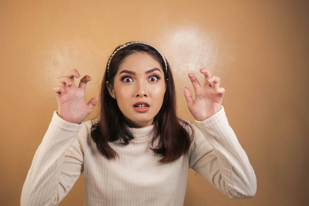 Beautiful Asian girl is mad and angry with arms fist isolated on orange background. - Photo, Image