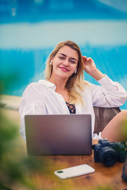 Belle femme photographe blogueuse en vacances, travaillant avec un ordinateur portable près de la piscine. Travail indépendant à distance - Photo, image
