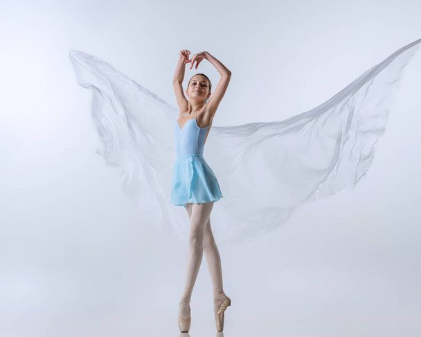 One young girl, aspiring ballerina in blue dress and pointes dancing with cloth isolated on gray background. Art, grace, beauty, ballet school concept - Foto, immagini