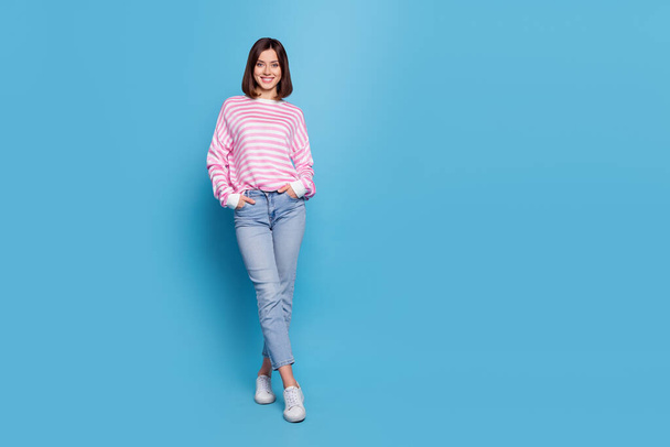 Full body photo of cute young lady stand wear shirt jeans footwear isolated on blue color background - 写真・画像