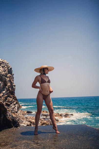 Bella ragazza bionda in costume da bagno in posa sulla spiaggia sulle rocce - Foto, immagini