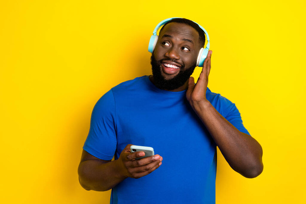 Portrait of handsome trendy cheerful guy listening melody chart using device isolated over bright yellow color background - Foto, immagini