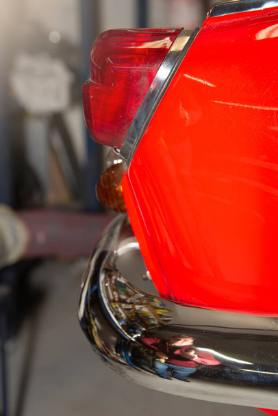 rood voertuig met een rode koplamp en een chromen bumper die de eigenaar weerkaatst en zwaait in een rood jasje - Foto, afbeelding