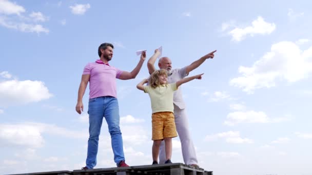 Niño con padre y abuelo sostienen aviones de papel apuntando con los dedos hacia el cielo, apuntan - Metraje, vídeo
