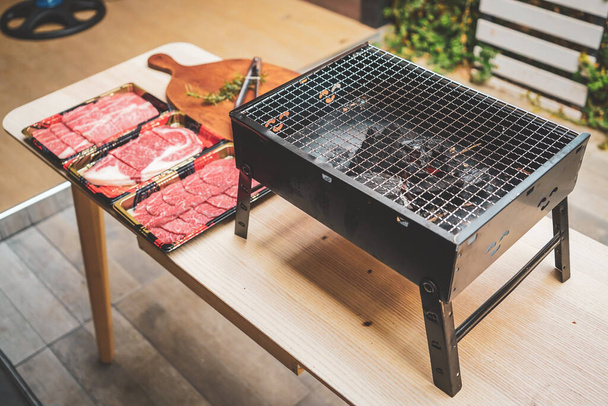 Close up of charcoal grill with raw sliced beef set on wooden table at Outdoor party. Home made barbecue beef grill smoke. - Φωτογραφία, εικόνα