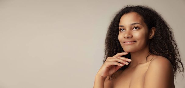 Close-up portrait of young beautiful woman with natural makeup and curly hair posing isolated over grey background - Foto, afbeelding