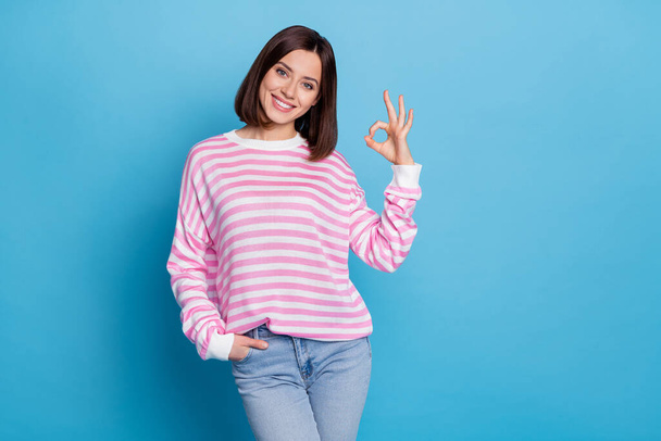 Photo of cute young lady show okey wear shirt jeans isolated on blue background - 写真・画像