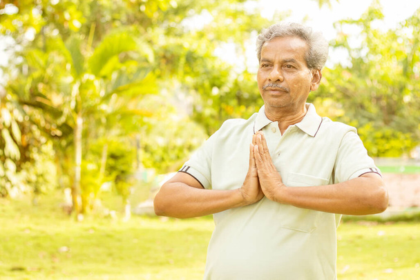 Senior-Mann in Namaste-Pose beim Yoga mit Kopierraum - Konzept für Fitness, aktiven gesunden Lebensstil und Morgenroutine. - Foto, Bild