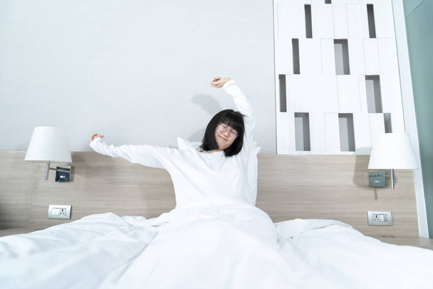 Klein Aziatisch jong bril meisje strekt zich uit op het bed in de ochtend met verfrissende en geluk. - Foto, afbeelding