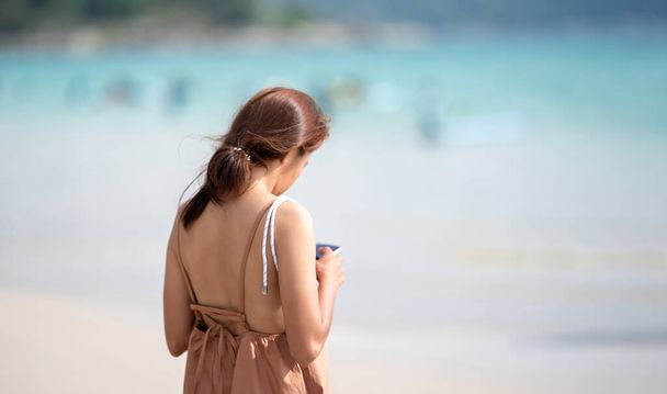 The shoulder of Asian Thai Woman from backside who play mobile at outdoor field sea beach blur background. - Photo, Image