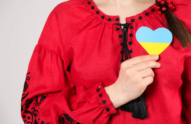 Egy piros hímzett inges ukrán nő szívet tart Ukrajna zászlajának színeiben. - Fotó, kép
