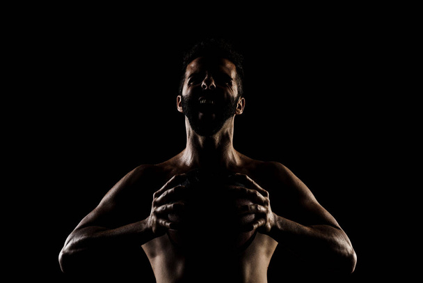 Basketball player holding a ball against black background. Side lit muscular Caucasian man silhouette. - Foto, immagini