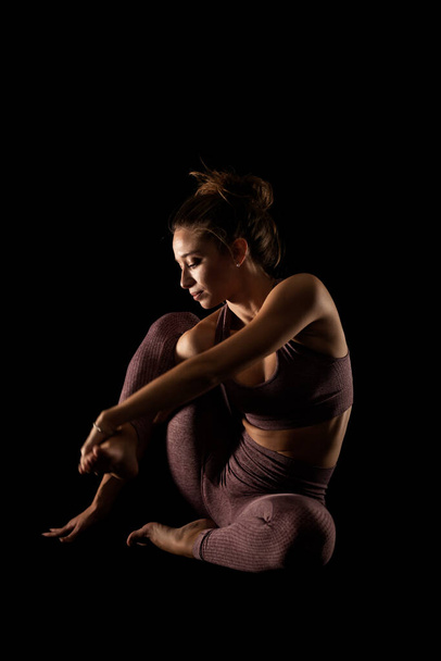Fit woman practicing yoga poses. Side lit half silhouette girl doing exercise in studio against black background. - Φωτογραφία, εικόνα