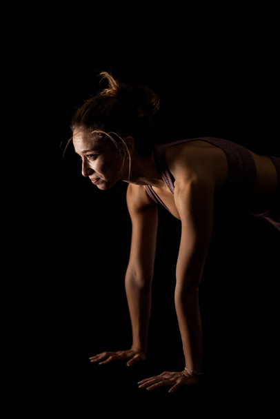 Fit woman practicing yoga poses. Side lit half silhouette girl doing exercise in studio against black background. - Fotó, kép