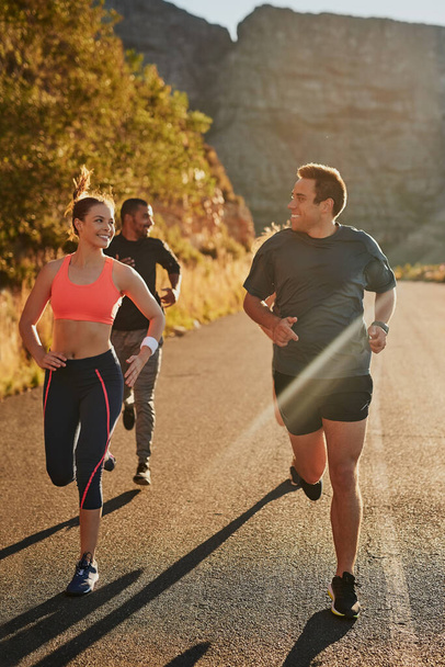 Se animan mutuamente a ir más rápido y más lejos. Foto de un grupo de fitness corriendo a lo largo de una carretera rural. - Foto, Imagen