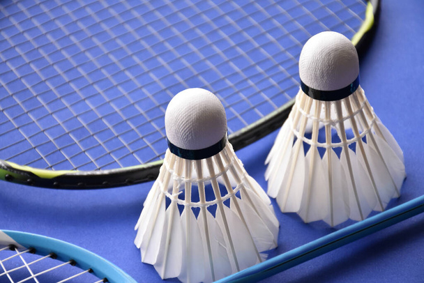 Badmintonschläger und weiße Federbälle auf blauem Boden des Badmintonhallenplatzes, Konzept für Badmintonliebhaber auf der ganzen Welt, weicher und selektiver Fokus. - Foto, Bild