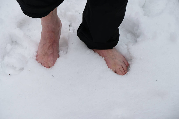 Senior walks barefoot on the snow. Bare sinewy male legs. Tempering exercises. Copy space. - Foto, immagini