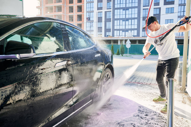 Boy cleaning auto by pressure water gun. - Фото, изображение
