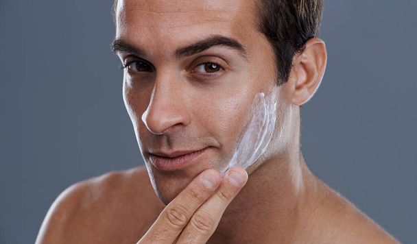 Zelfs mannen willen graag zacht zijn..... Studio shot van een knappe jongeman van toepassing crème in zijn gezicht. - Foto, afbeelding