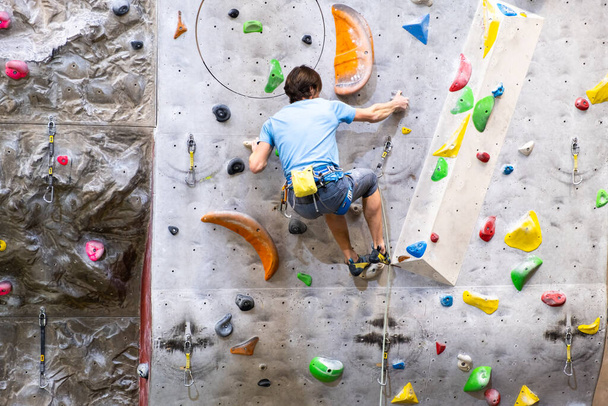 The climber trains on the artificial rock wall with insurance in bouldering gym - Valokuva, kuva