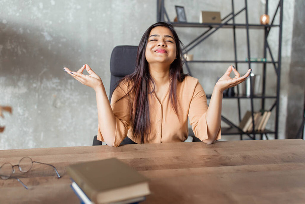 Young indian girl wearing casual clothes sitting on the table relaxed and with eyes closed during meditation gesture with - 写真・画像
