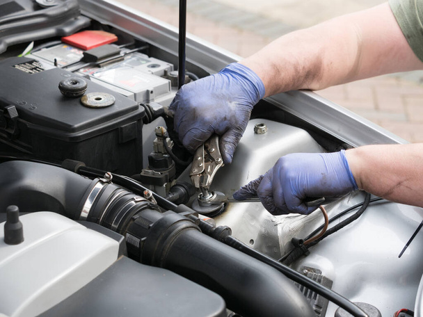 Paar mechanische Hände mit blauen Handschuhen, die im Motorraum eines Sportwagens mit Zangengriff und Schraubenschlüssel arbeiten. - Foto, Bild