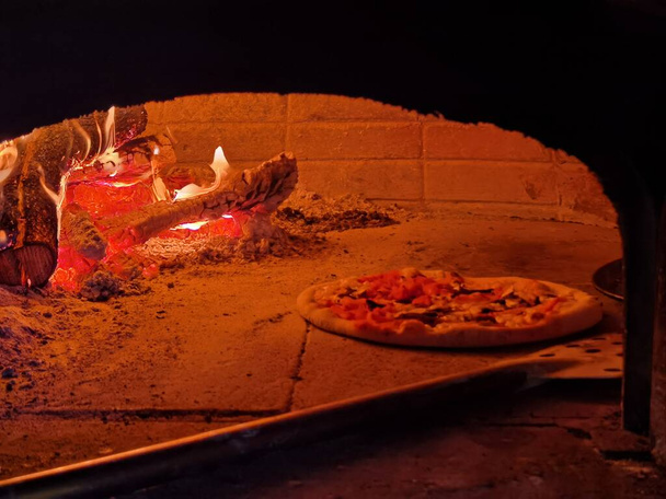 comida de pizza caliente en el horno con maderas y fuego fresco preparación cocina interior - Foto, Imagen