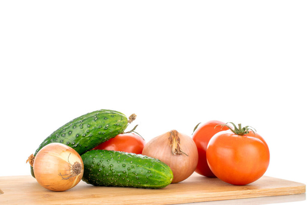 Drie rijpe tomaten, twee uien en twee komkommers op een houten snijplank, macro, geïsoleerd op een witte achtergrond. - Foto, afbeelding