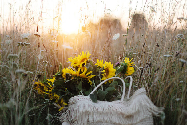 Beaux tournesols en sac de paille dans la prairie d'été dans la lumière du coucher du soleil chaud. Moment atmosphérique tranquille dans la campagne. Rassemblement bouquet de tournesols parmi les fleurs sauvages dans le champ du soir - Photo, image