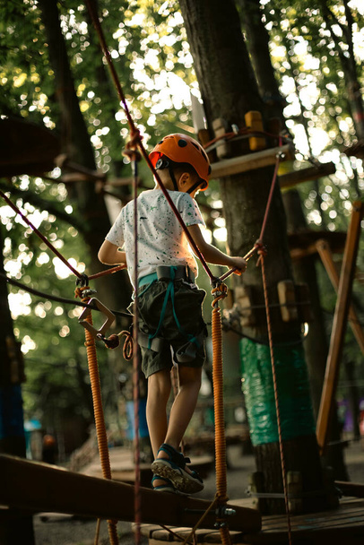 A cheerful boy in an orange helmet has fun in the rope park - 写真・画像