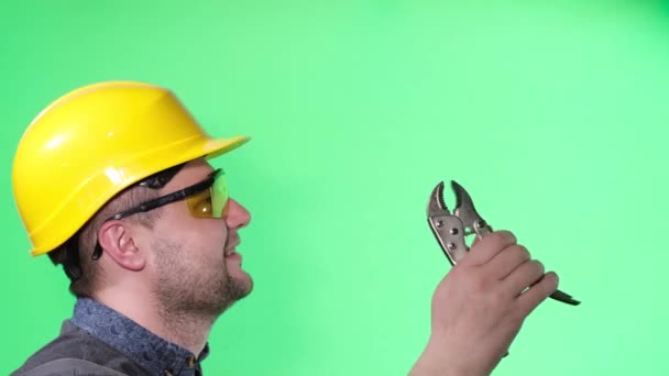 Μηχανικός εργάτης κρατώντας πένσα στο πράσινο φόντο, κοιτάζει στο πλάι - Πλάνα, βίντεο
