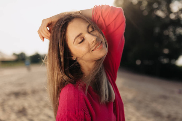 Lähikuva romanttinen muotokuva ihana tyttö tummat hiukset koskettaa hiuksia ja hymyilee tarkasti taustalla hiekkaranta auringonpaisteessa. Laadukas kuva - Valokuva, kuva