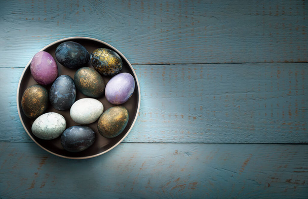 Easter colored eggs in a dish on a blue wooden background. Place for text. - Фото, зображення